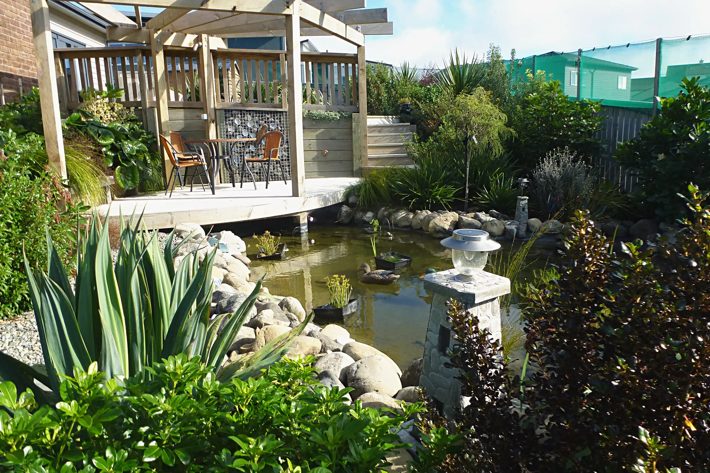 Pond edged with boulders below a timber pergola deck, Aotea
