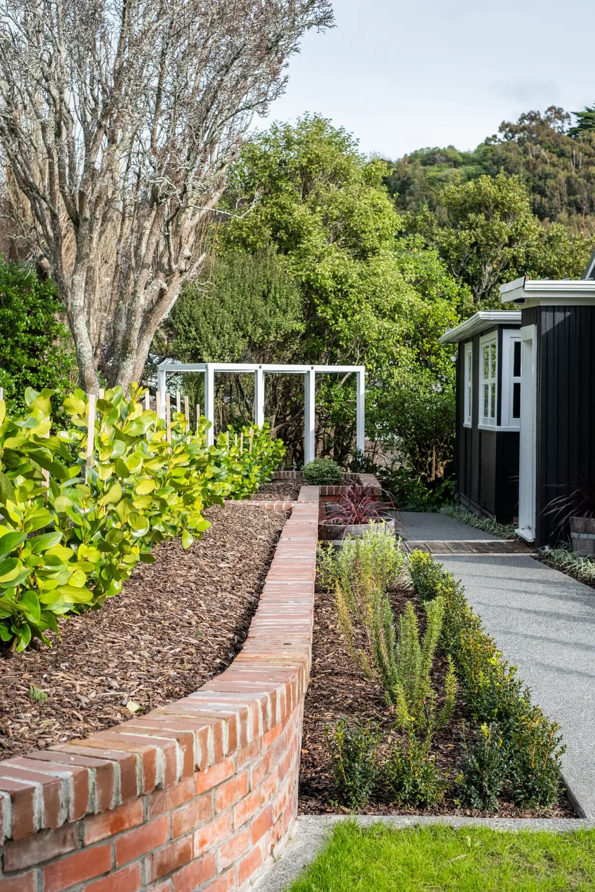 Paremata Road - A waterfront lawn rebuilt into outdoor rooms: a fireplace terrace, curved brick walls, a pergola walkway and new planting above the water.